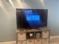 TV powered on showing no signal message, placed on a wooden media console with fabric storage bins below.