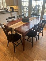 Dining table with six black dining chairs in a kitchen setting, natural light illuminates the cherry wood finish of the table.