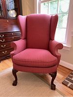 Front view of large wing chair showing dark raspberry patterned upholstery and ball-claw feet on front legs.