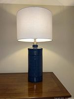 Photo of the blue ceramic lamp illuminated on a wooden table showing texture and shape of base and shade