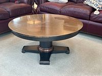 Copper top of the coffee table showing warm patina and spots with the black metal base partially visible, positioned on a gray carpet near leather seating.