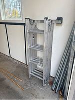Side view of folded ladders leaning against a garage wall, showing aluminum construction and condition