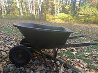 Side view of wheelbarrow showing black metal basin, wooden handles, single black tire, and metal supports.