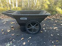 Side view of black Rubbermaid plastic wheelbarrow showing large wheel and basin shape.