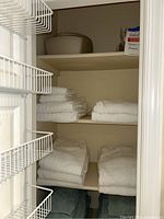 Closet shelf with multiple stacks of white towels folded neatly.