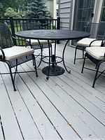 Full side view of the round wrought iron outdoor dining table with chairs around it on a deck.