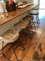 Four rustic wood and black metal bar stools positioned under a wooden bar counter on wooden flooring.