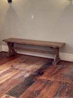 Natural finish wooden bench showing simple triangular leg supports and horizontal crossbeam, placed on distressed wood floor.