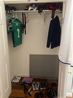 Wide view of closet showing hanging jerseys, jacket, shoes on floor, and folded clothes on shelf