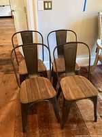 Front view of four metal and wood dining chairs arranged in two rows, showing dark metal frames and wooden seats on a wooden floor.