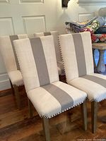 Set of four upholstered wood dining chairs with beige and light gray vertical striped fabric and nailhead trim, arranged on wooden floor