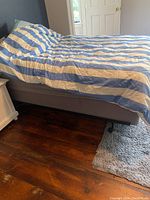 Full view of full size bed frame covered by striped comforter and pillows