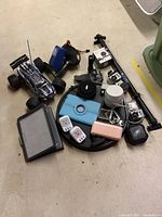 Wide view of lot items on floor showing GoPro cameras, RC car, remote controller with attached charger, charging bricks, cables, mounts, and power adapters
