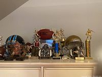 Full view showing Tennessee Titans helmet, Notre Dame helmet, multiple football trophies, and cased football.