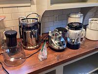 Photo showing entire lot of kitchen appliances on wood counter including Dash juicer, Cuisinart food processor, blender, and white Cuisinart ice cream maker with manual.
