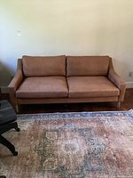 Full view of brown leather sofa showing seating and armrests with cushions placed on top.