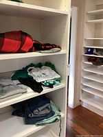 Shelves with folded men's shirts including white, gray, green, and blue jeans stacked on lower shelves. Hats visible on adjacent shelves.