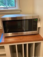 Full view of Sharp Carousel microwave oven on wooden shelf under window.