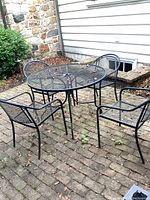 The full set includes an oval cast iron mesh patio table with four matching chairs. The set is on a brick patio with signs of weathering and leaf debris on the surfaces.