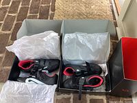 Overview of two pairs of Peloton cycling shoes black with red lining in original boxes with tissue paper lined.