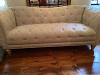Front view of beige tufted sofa showing button details and wooden legs