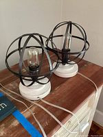 Two metal sphere lamps side by side on a wooden surface showing their full form and bases