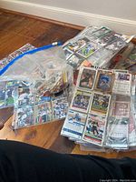 Pile of assorted cards in binder pages and a clear resealable bag on wooden floor