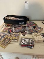 Multiple stacks of basketball and football cards spread across a table with a Maxell storage bag in background