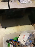 Samsung 40-inch TV on floor with a plastic bin of LEGO pieces and manual visible nearby.