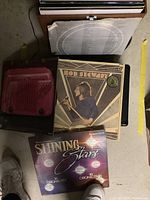 Photo of vinyl albums including Rod Stewart Greatest Hits and Shining Stars compilation, showing album covers on floor