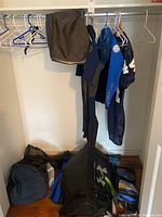 Closet with wetsuits, beach shorts hanging and bags with fins on the floor.