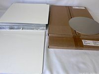 Photo showing two stacks of flat, rectangular aluminum panels with white surfaces and some cardboard packaging, indicating the lot includes sheets in sets and sizes.
