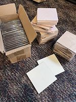 Photo showing boxed stack of glossy white MDF coaster blanks and loose natural pine coaster blanks in piles, on carpet.