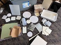 Overview of assorted sublimation blanks including various shaped coasters, photo panels, cork sheets, mug, and trays laid on carpeted floor.