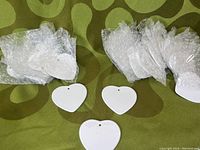 24 individually wrapped glossy white ceramic heart-shaped ornaments with small holes for hanging, displayed on green patterned surface