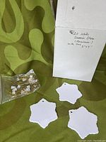 White ceramic star-shaped ornaments displayed alongside a package with handwritten note '20 white ceramic stars (porcelain) white tier 3"x3"' and clear bags containing hanging ribbons.