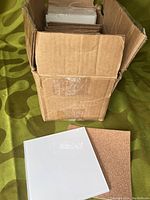 Box with stack of frosted glass tiles and cork backings visible, one tile and one cork backing outside the box.