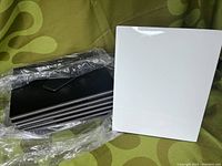 Stack of glossy white photo panels with visible black edges and easels wrapped in plastic on a green patterned background.