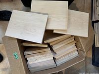 Box filled with natural pine flat panels, mostly uniform size 8x10 inches with some smaller and larger pieces visible. Light natural wood grain. Panels arranged in a cardboard box.