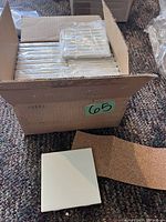 Box containing multiple stacks of individually wrapped matte white ceramic tiles.