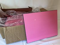Set of six MDF panels with glossy white fronts covered by pink protective film, black edges and backs, propped against a cardboard box with packaging materials.