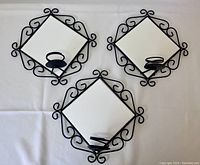 Photo showing three black metal candle sconces with attached circular candle holders and removable white tiles placed diagonally. Decorative curls on metal frame are visible. White tiles are blank and glossy.