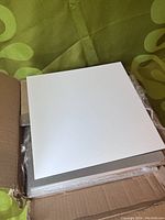 Top view of aluminum panels with a glossy white finish stacked inside an open cardboard box, showing smooth white surfaces.