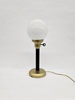 Front view of the Art Deco table lamp showing the frosted glass globe shade and brass base with black neck on a white background.