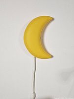 Front view of yellow crescent moon shaped wall lamp, showing smooth plastic surface and crescent shape.