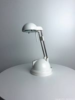 White Espressivo halogen desk lamp with dome-shaped head and base, telescoping and flexible adjustable arm shown folded and extended