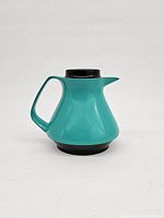 Side profile view of turquoise insulated carafe with handle and spout visible, black lid on top.