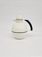 Front and side view of one white spherical MCM insulated carafe with black handle and spout lid shaped like a penguin.
