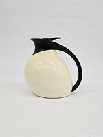 Front view of one white Stelton insulated thermos carafe shaped like a bird, showing off-white glossy body with black handle and spout lid.
