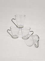 Four clear glass coffee cups stacked and arranged featuring removable stainless steel handles and bases.